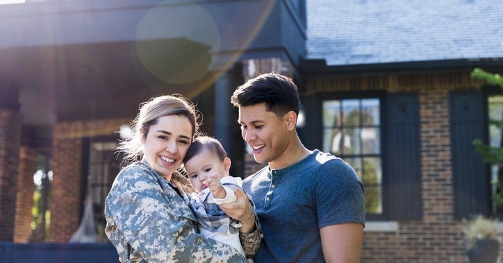 A young military veteran standing in front of her home with her baby and husband.
