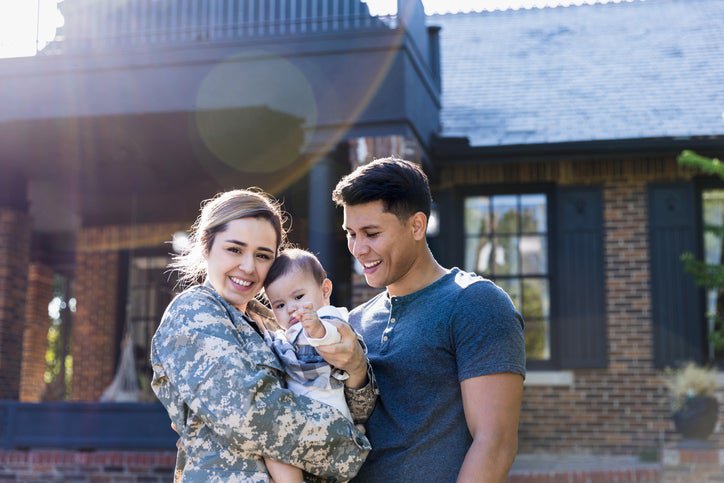 A young military veteran standing in front of her home with her baby and husband.