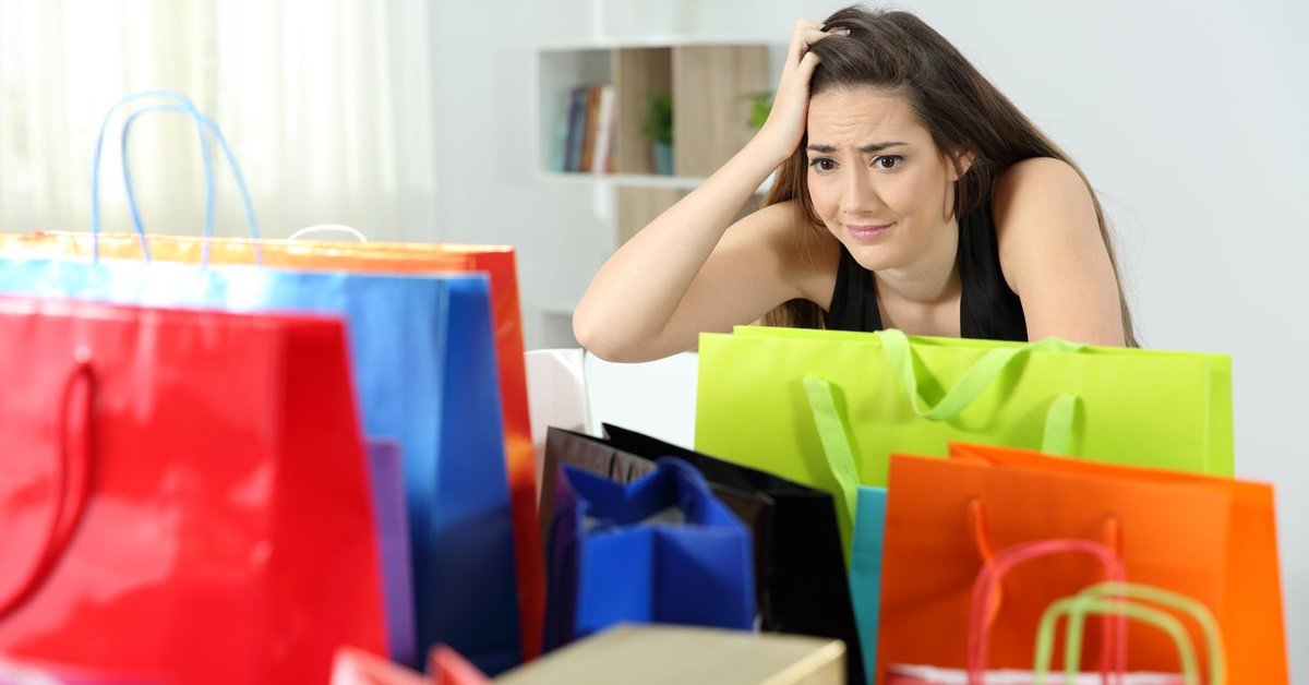 A woman with a concerned look on her face sits looking at a bunch of shopping bags.