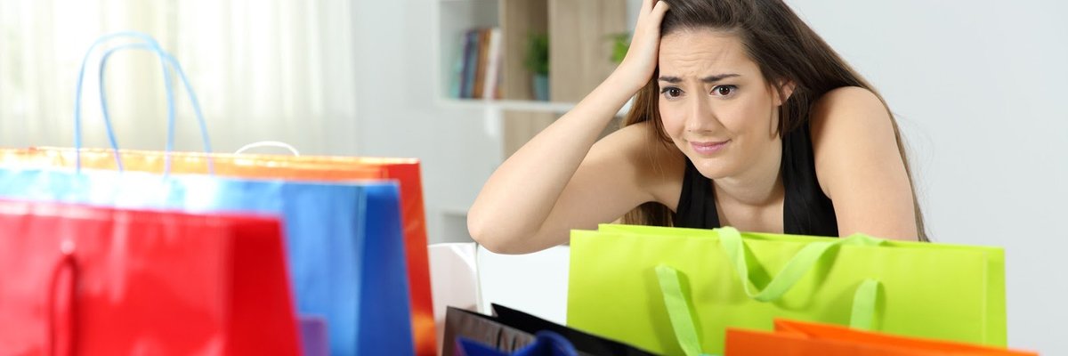 A woman with a concerned look on her face sits looking at a bunch of shopping bags.