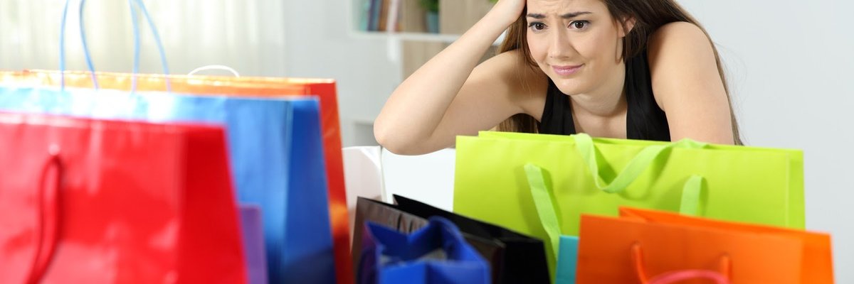 A woman with a concerned look on her face sits looking at a bunch of shopping bags.