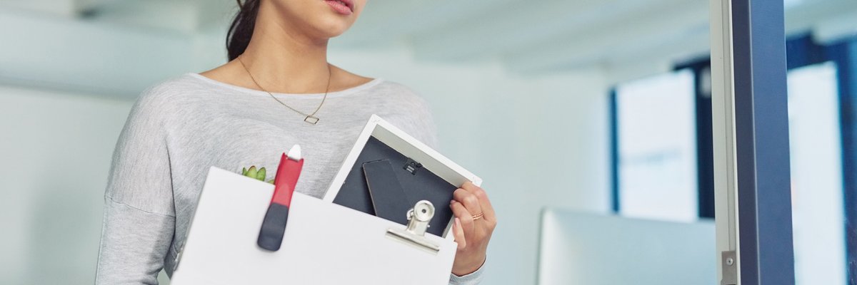 A young woman who was just let go from her job walking out of the office with a box of her things.