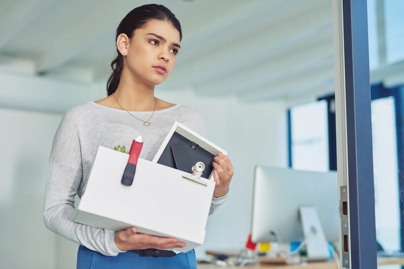 A young woman who was just let go from her job walking out of the office with a box of her things.