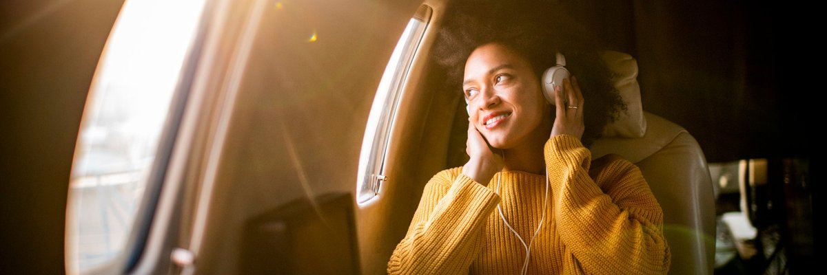 A smiling airplane passenger listening to music and looking out the window.