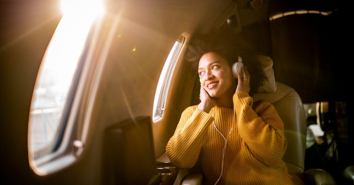 A smiling airplane passenger listening to music and looking out the window.