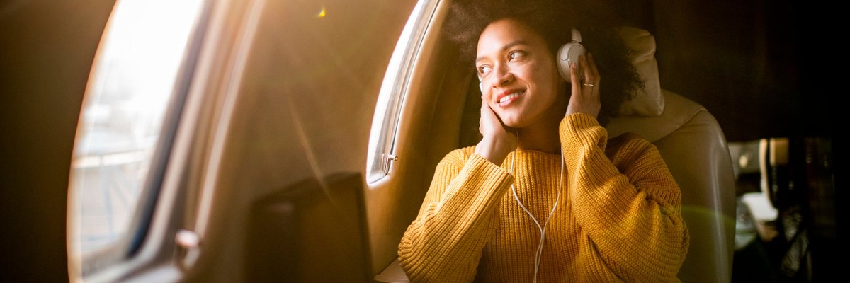 A smiling airplane passenger listening to music and looking out the window.