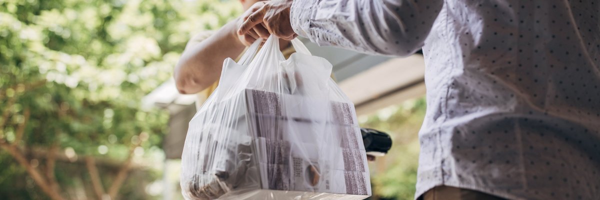 A delivery man handing over a bag of takeout food to a customer.