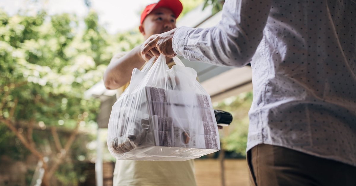 A delivery man handing over a bag of takeout food to a customer.
