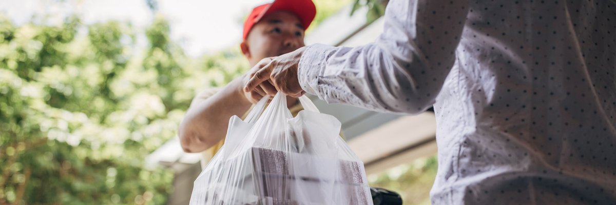 A delivery man handing over a bag of takeout food to a customer.