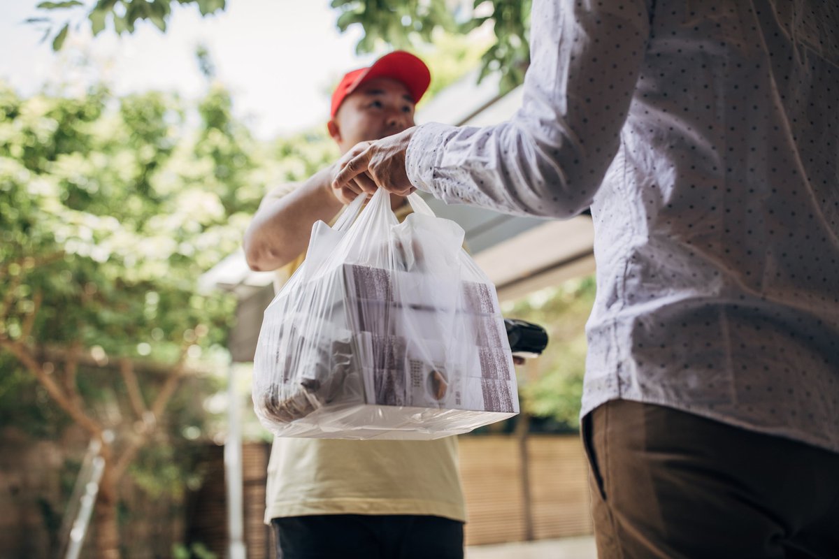 A delivery man handing over a bag of takeout food to a customer.