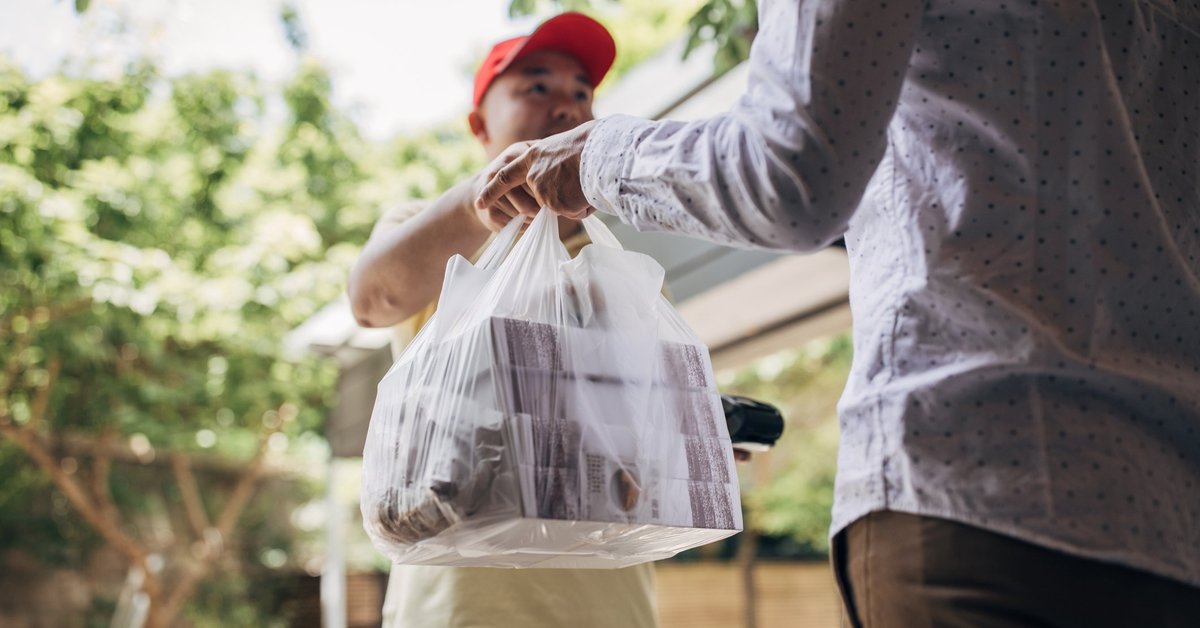 A delivery man handing over a bag of takeout food to a customer.