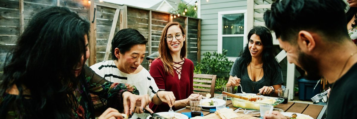 A group of friends eating a meal around a backyard patio table.