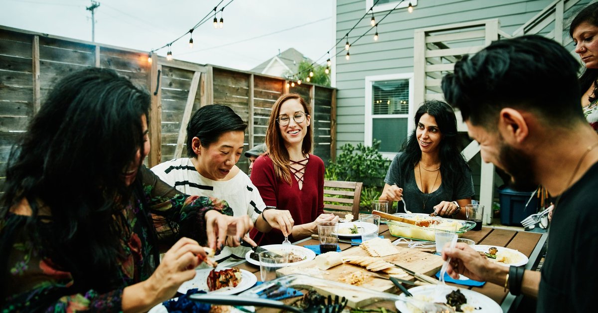 A group of friends eating a meal around a backyard patio table.