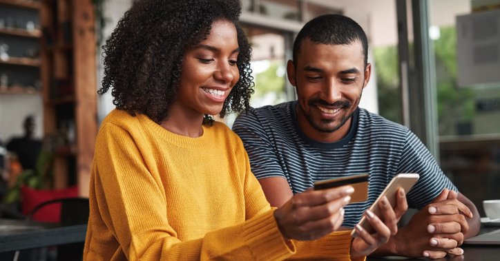 A man and a woman looking at a phone and a credit card.