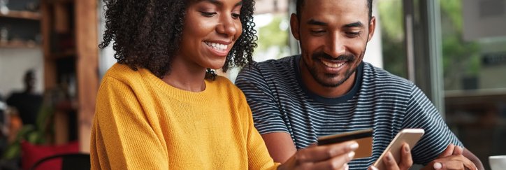 A man and a woman looking at a phone and a credit card.