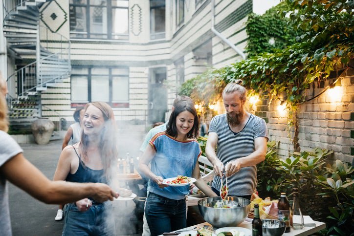 A group of friends cooking at a barbecue in the shared courtyard of an apartment building.
