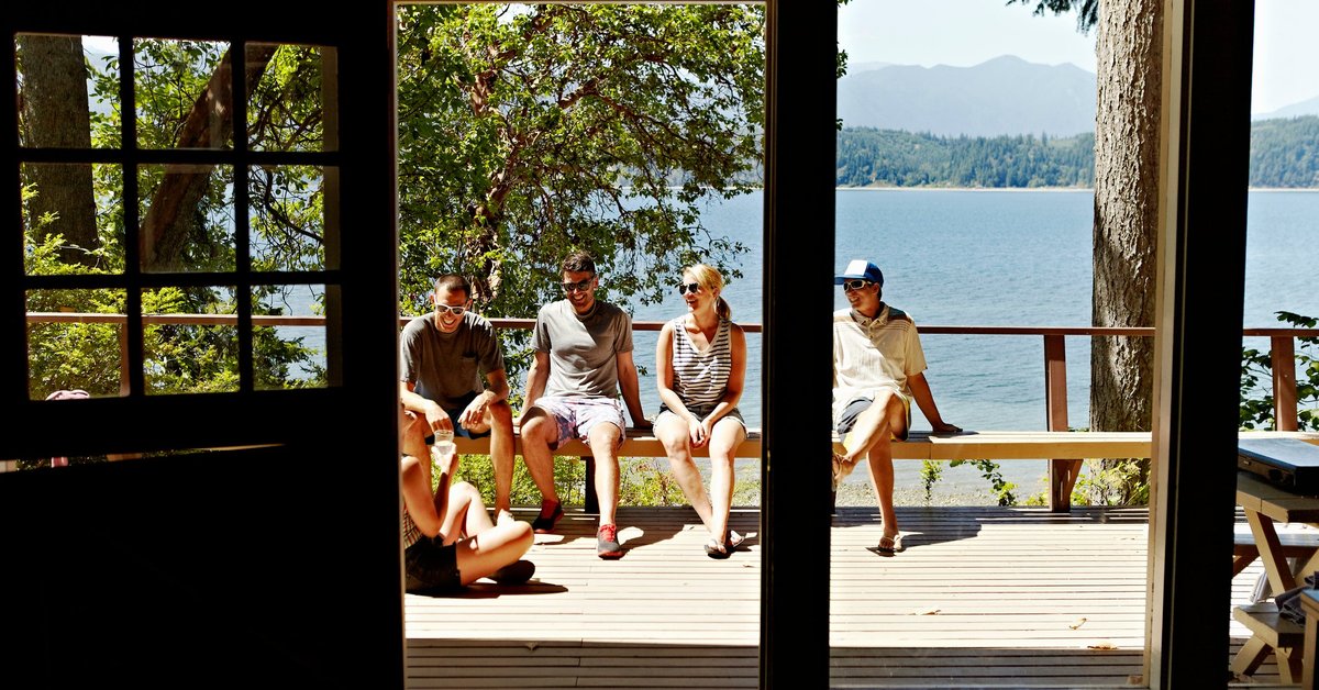 A group of friends sitting in the sun on the deck of a lakefront cabin.