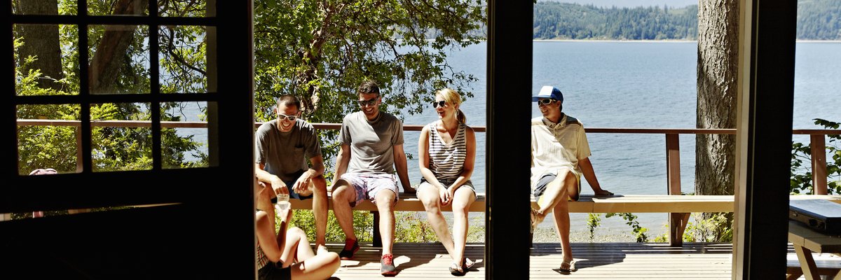 A group of friends sitting in the sun on the deck of a lakefront cabin.