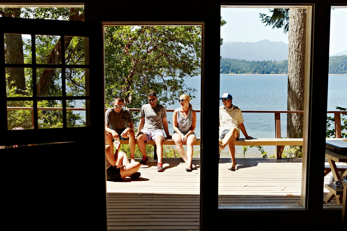 A group of friends sitting in the sun on the deck of a lakefront cabin.