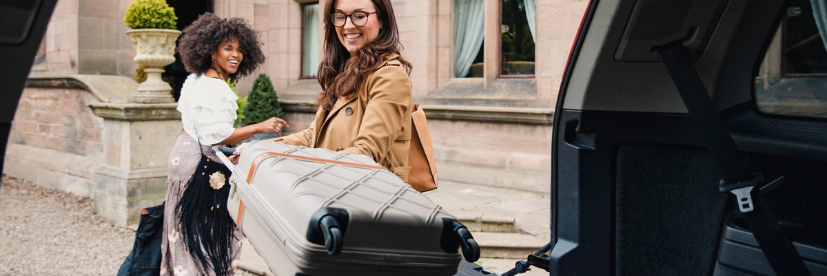 Two people unloading luggage from the back of a vehicle.