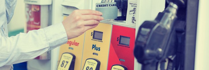 A hand placing a credit card into a gas pump card reader.