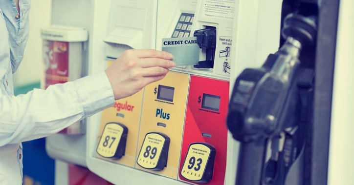 A hand placing a credit card into a gas pump card reader.