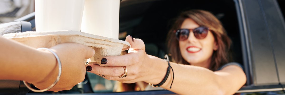 Person being handed coffees at a drive-thru window.