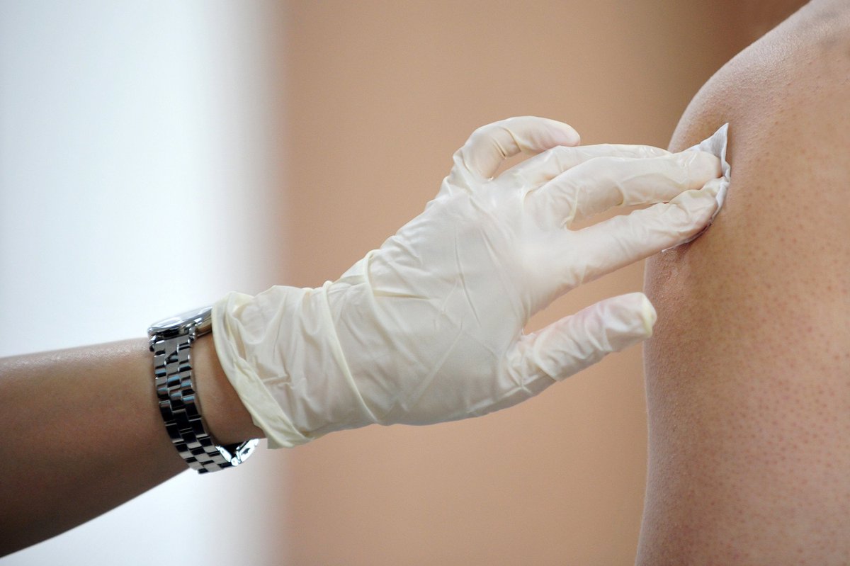 Gloved medical worker rubbing alcohol on vaccine injection site on arm of patient.