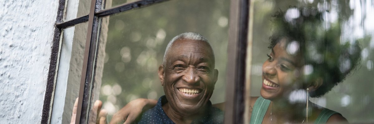A smiling grandfather and his adult granddaughter looking out of window at the trees.