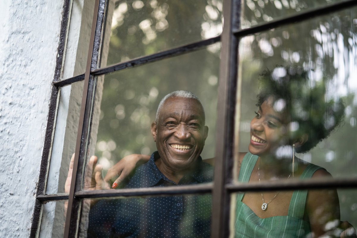A smiling grandfather and his adult granddaughter looking out of window at the trees.