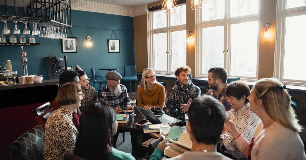 A group of people sitting in a circle of chairs having a social meeting at a restaurant.