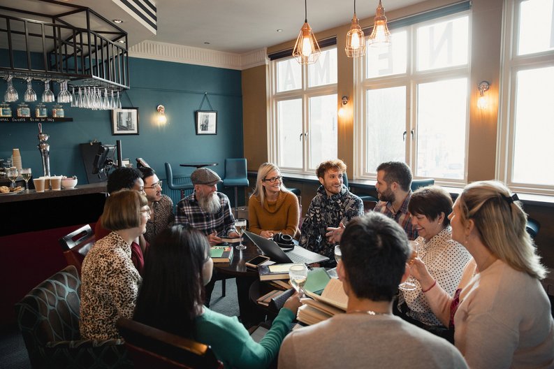 A group of people sitting in a circle of chairs having a social meeting at a restaurant.
