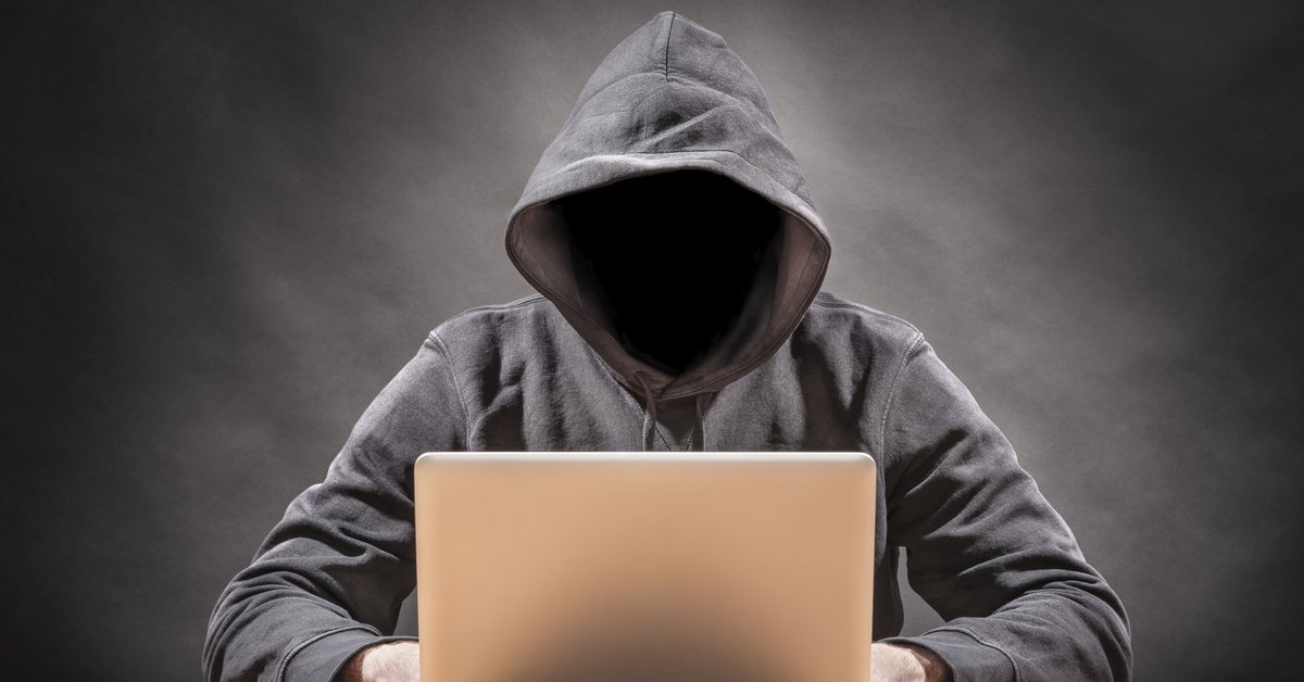 Man wearing hoodie with his face in shadow using a laptop.