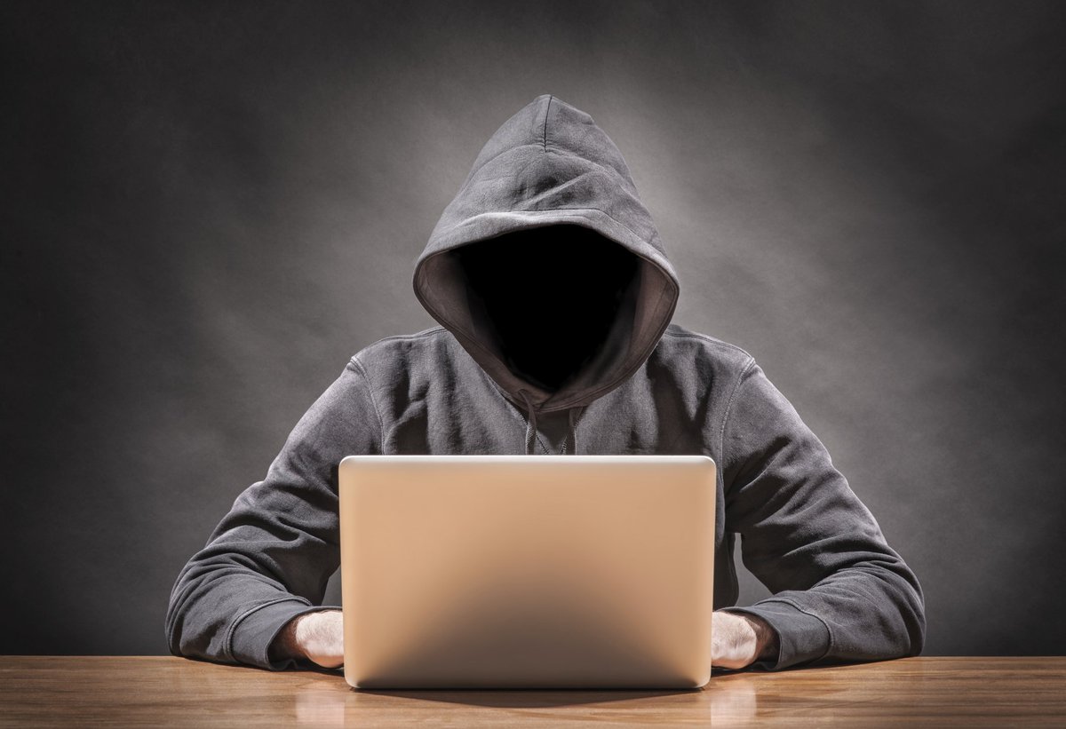 Man wearing hoodie with his face in shadow using a laptop.