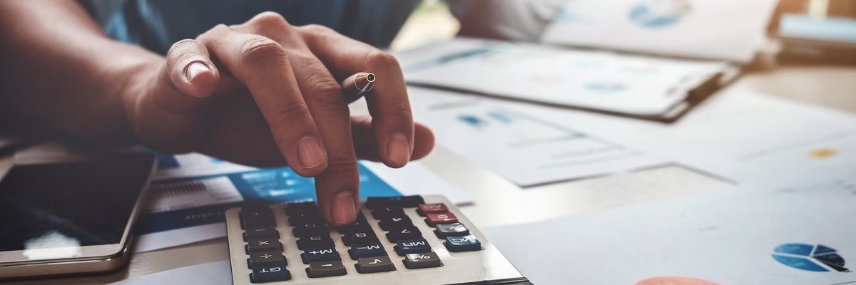 hand typing on calculator with papers in background