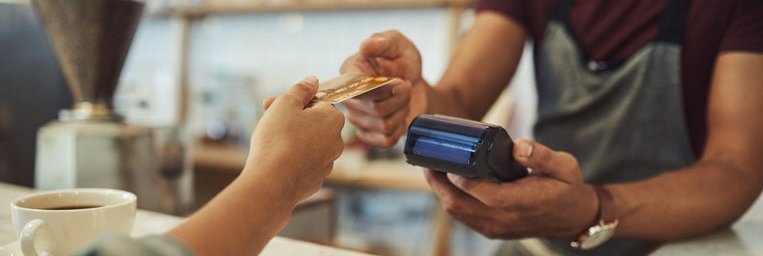 A hand holding a credit card out to a cashier behind the counter at a cafe.