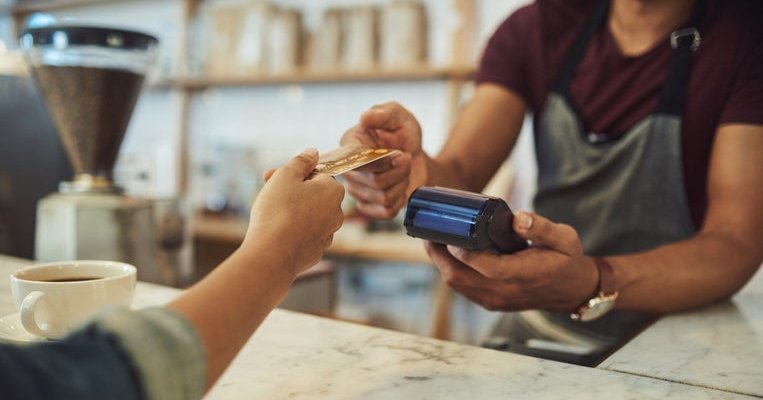 A hand holding a credit card out to a cashier behind the counter at a cafe.