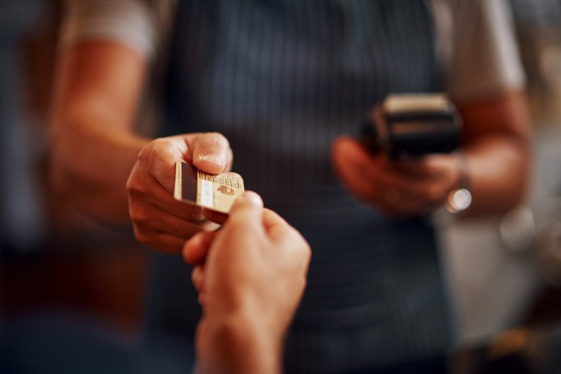 A hand passing a credit card to an employee holding a card payment device.