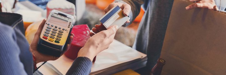A woman holding a shopping bag and handing her credit card to the store cashier.