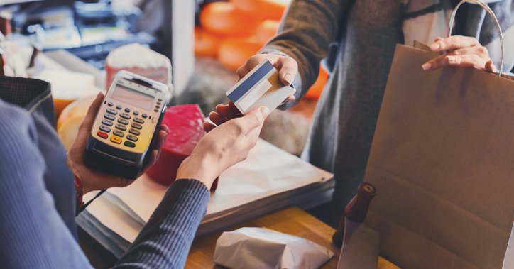 A woman holding a shopping bag and handing her credit card to the store cashier.