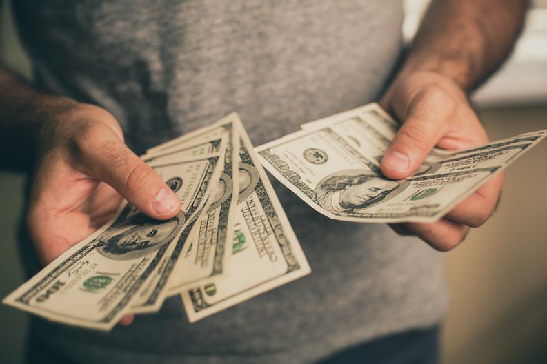 A man holding several hundred dollar bills in his hands,