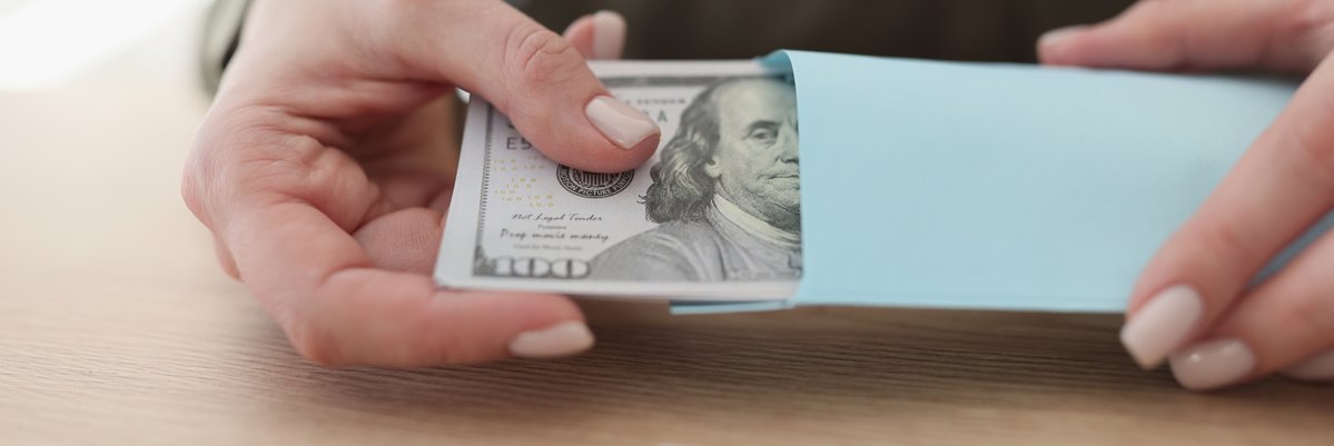 A person sitting at a table holding an envelope full of hundred-dollar bills.