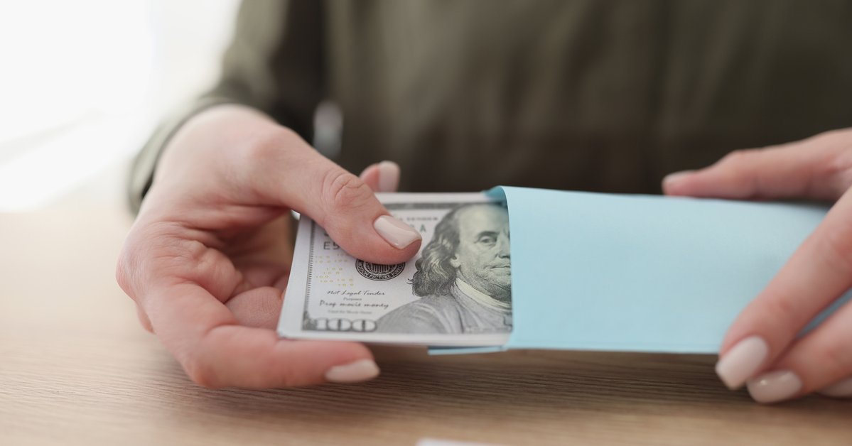 A person sitting at a table holding an envelope full of hundred-dollar bills.