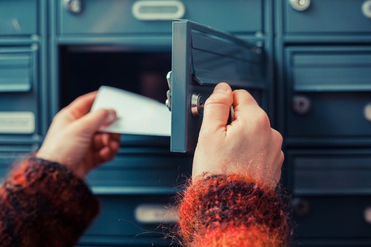 A woman's hands opening a mailbox and pulling out an envelope.
