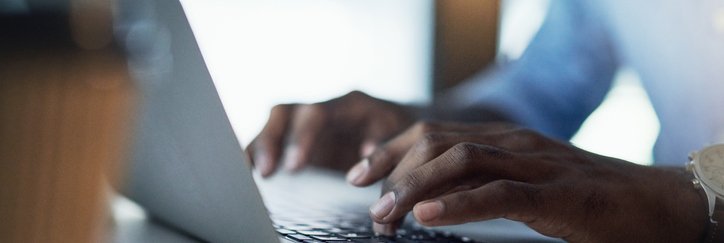 A man's hands typing on a laptop keyboard.