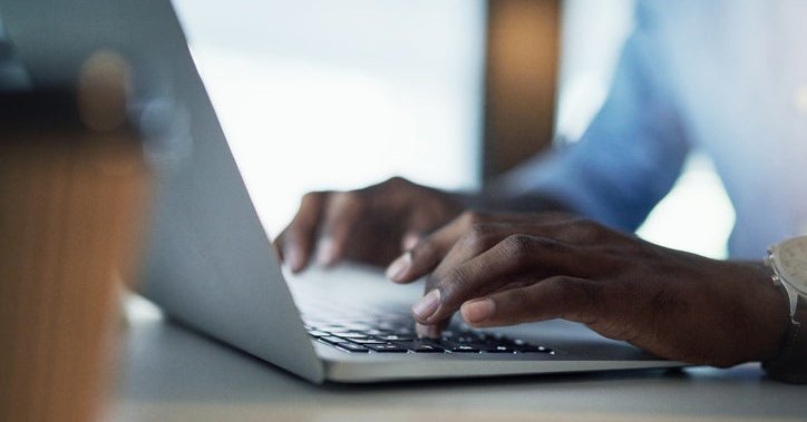A man's hands typing on a laptop keyboard.