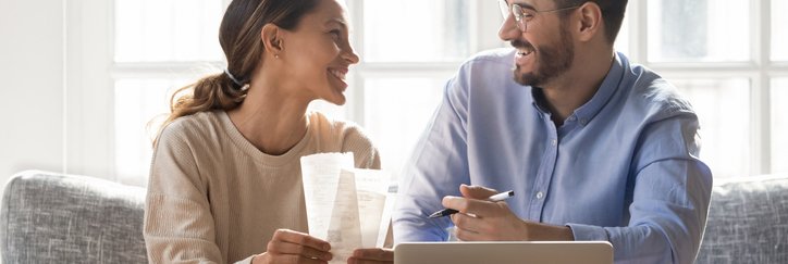 A happy couple on a couch with receipts and a laptop.