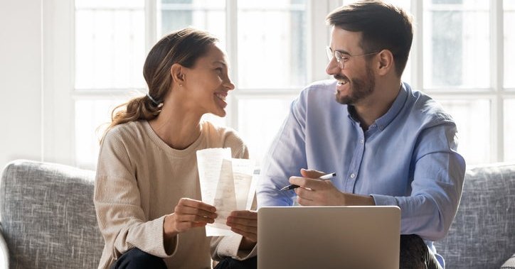 A happy couple on a couch with receipts and a laptop.