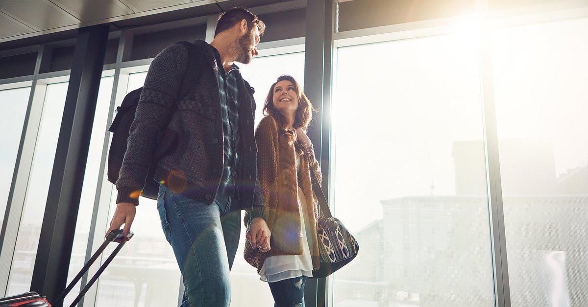 A happy couple holding hands while walking in an airport.