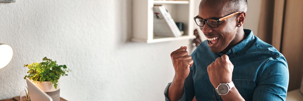 An excited person in glasses looking at laptop screen and celebrating.